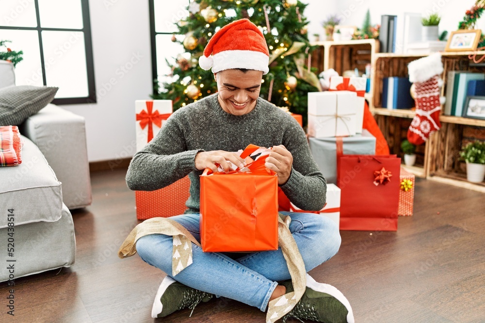 © Krakenimages.com - Young hispanic man unpacking gift sitting by christmas tree at home © Krakenimages.com - Young hispanic man unpacking gift sitting by christmas tree at home