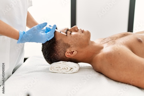 Young hispanic man relaxed having antiaging treatment at beauty center