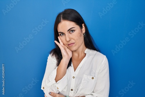Young hispanic woman standing over blue background thinking looking tired and bored with depression problems with crossed arms.