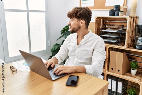 Young arab man working using computer laptop at the office looking to side, relax profile pose with natural face with confident smile.