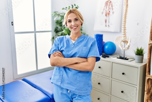 Beautiful blonde physiotherapist woman working at pain recovery clinic happy face smiling with crossed arms looking at the camera. positive person.
