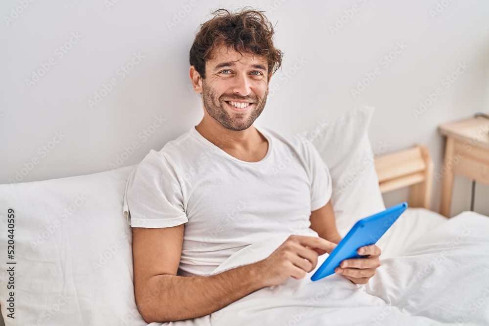 Young man using touchpad sitting on bed at bedroom Young man using touchpad sitting on bed at bedroom