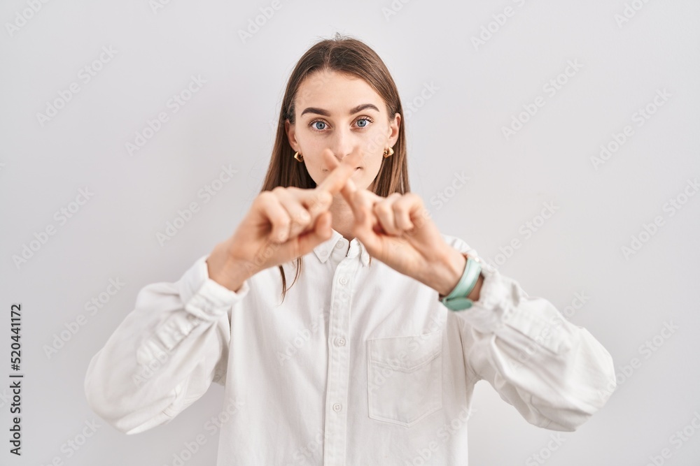 Young caucasian woman standing over isolated background rejection expression crossing fingers doing negative sign Young caucasian woman standing over isolated background rejection expression crossing fingers doing negative sign