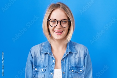 Young caucasian woman standing over blue background with a happy and cool smile on face. lucky person.