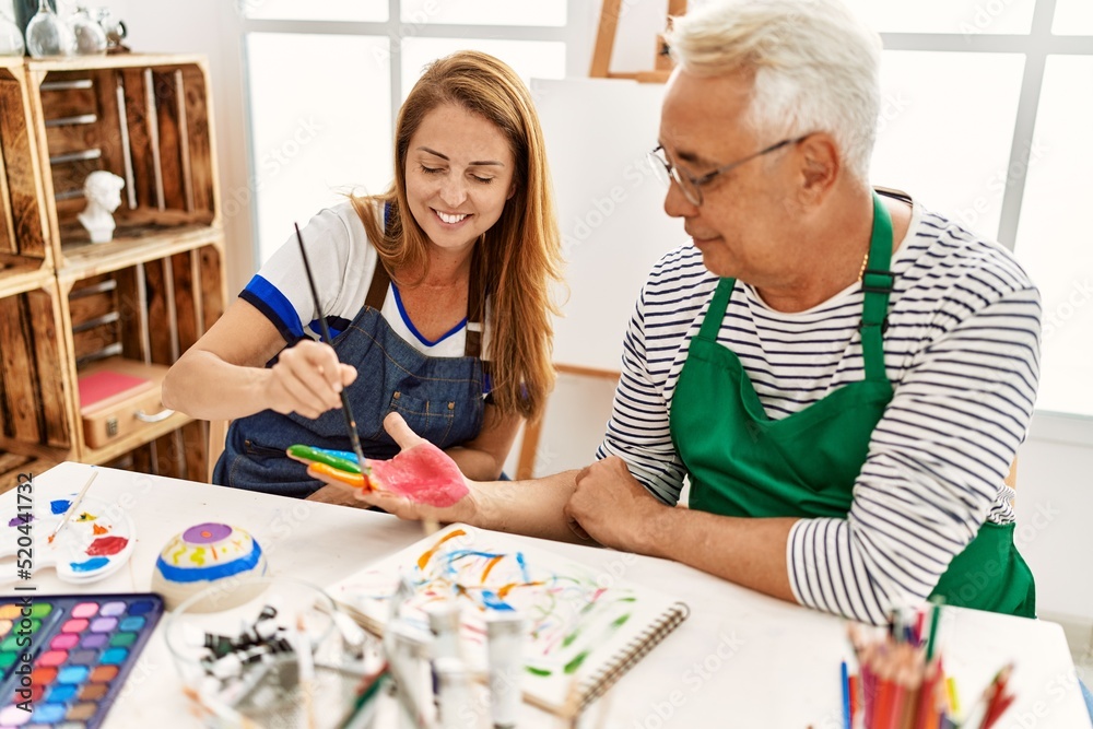 Fototapeta premium Two middle age artists smiling happy painting hands at art studio.