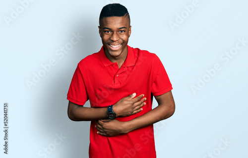Young african american man wearing casual red t shirt smiling and laughing hard out loud because funny crazy joke with hands on body.