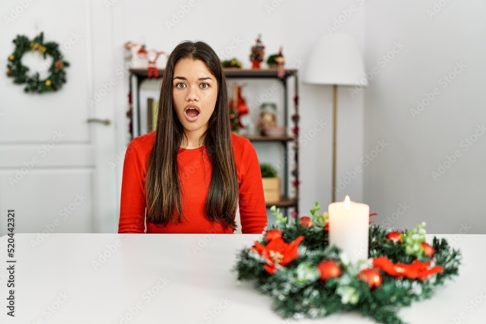 Young brunette woman sitting on the table on christmas scared and amazed with open mouth for surprise, disbelief face Young brunette woman sitting on the table on christmas scared and amazed with open mouth for surprise, disbelief face