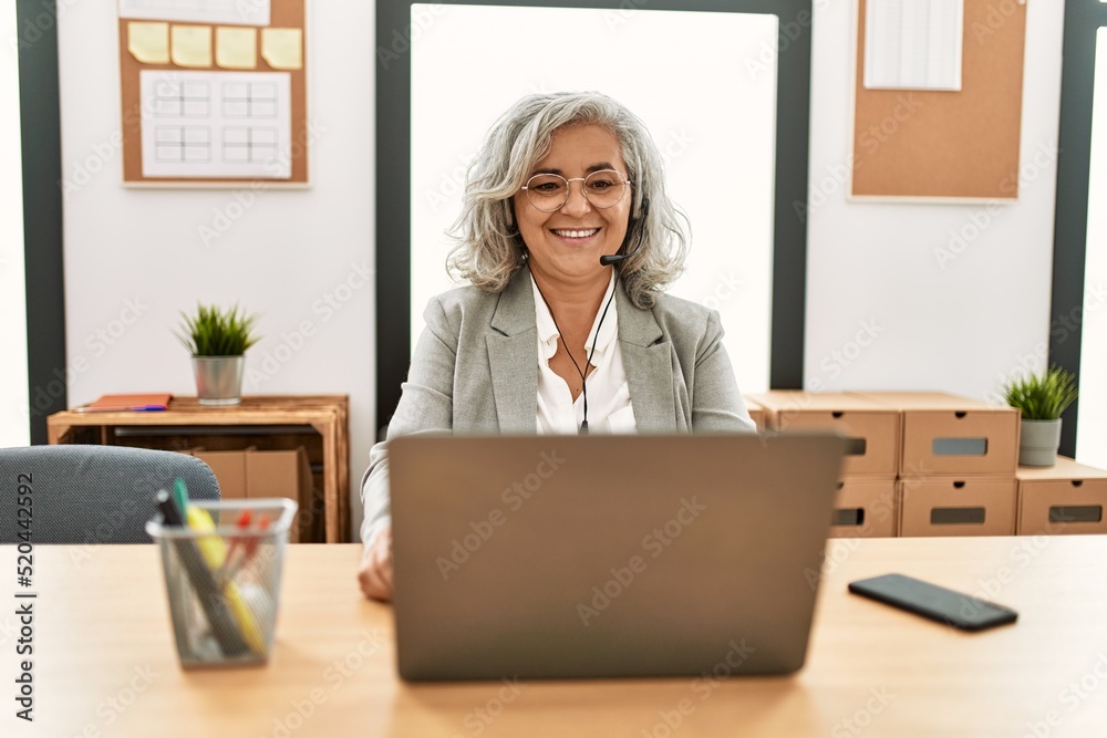 Middle age businesswoman sitting on desk working using laptop at office with a happy and cool smile on face. lucky person. Middle age businesswoman sitting on desk working using laptop at office with a happy and cool smile on face. lucky person.