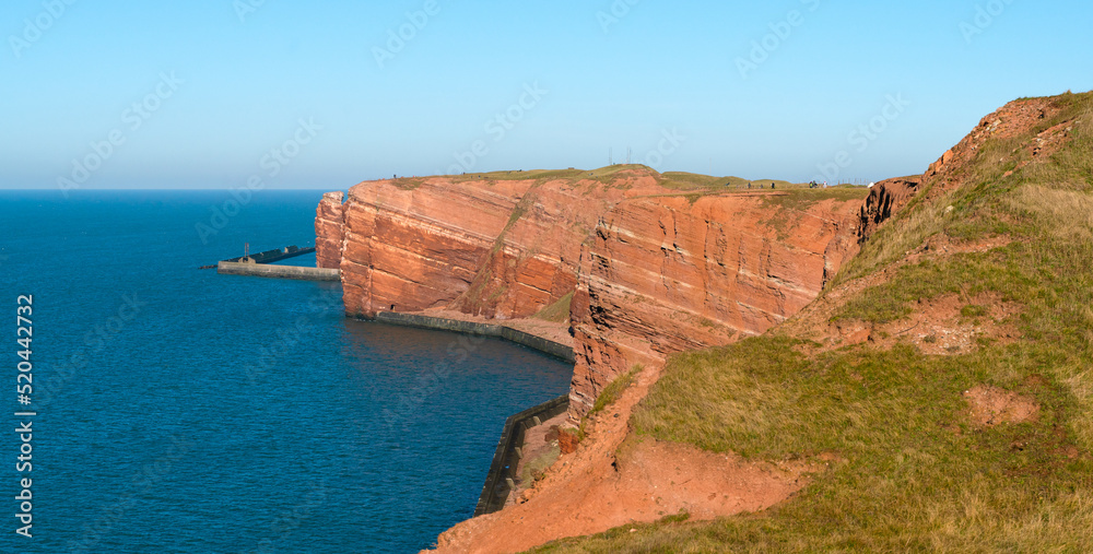 Tall red dramatic cliffs of Heligoland island with on a beautiful sunny day. Winter day in Helgoland in the North sea, Germany. Blue waters and red rock cliffs.