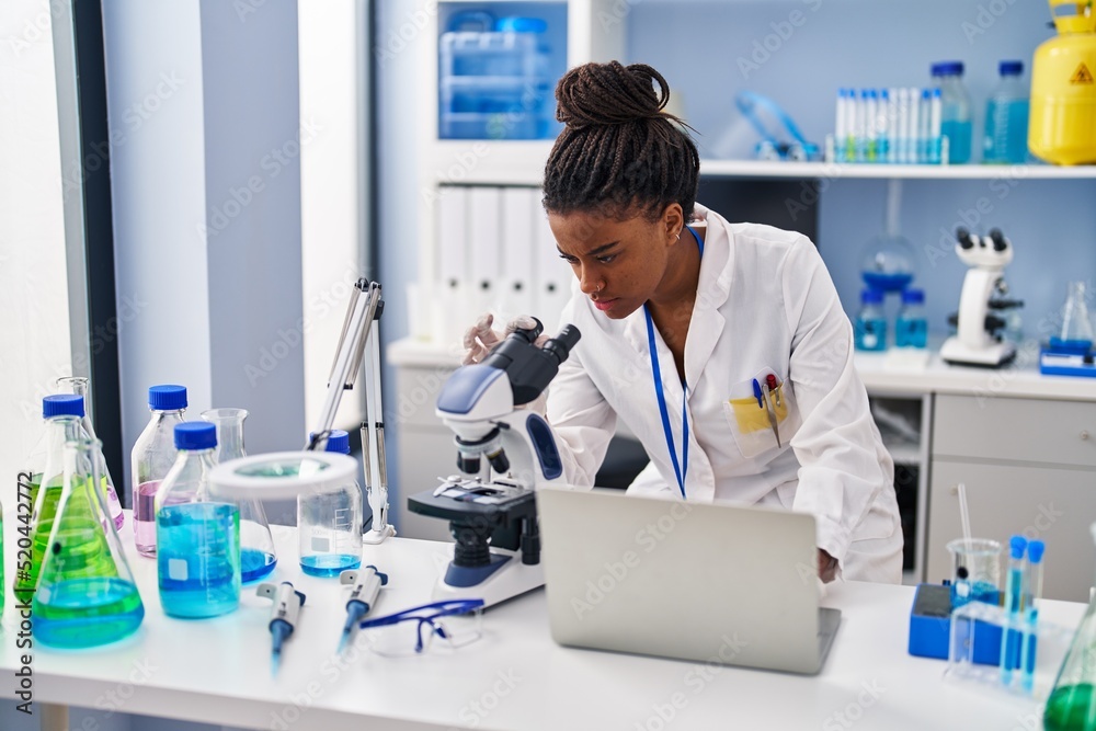 African american woman scientist using laptop and microscope at laboratory African american woman scientist using laptop and microscope at laboratory