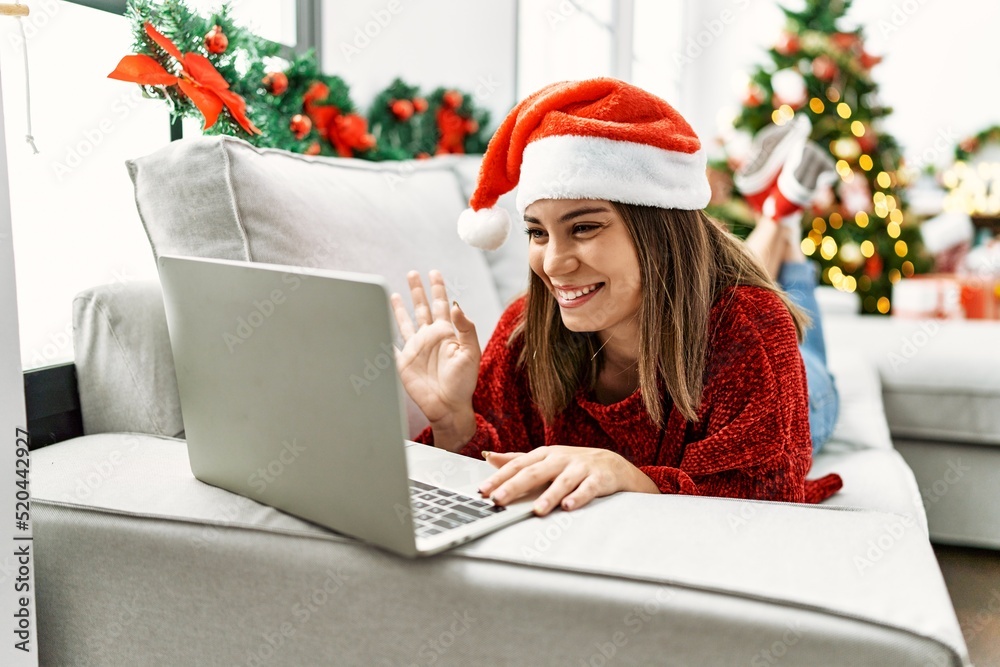 Young hispanic girl having video call lying on the sofa by christmas tree at home. Young hispanic girl having video call lying on the sofa by christmas tree at home.