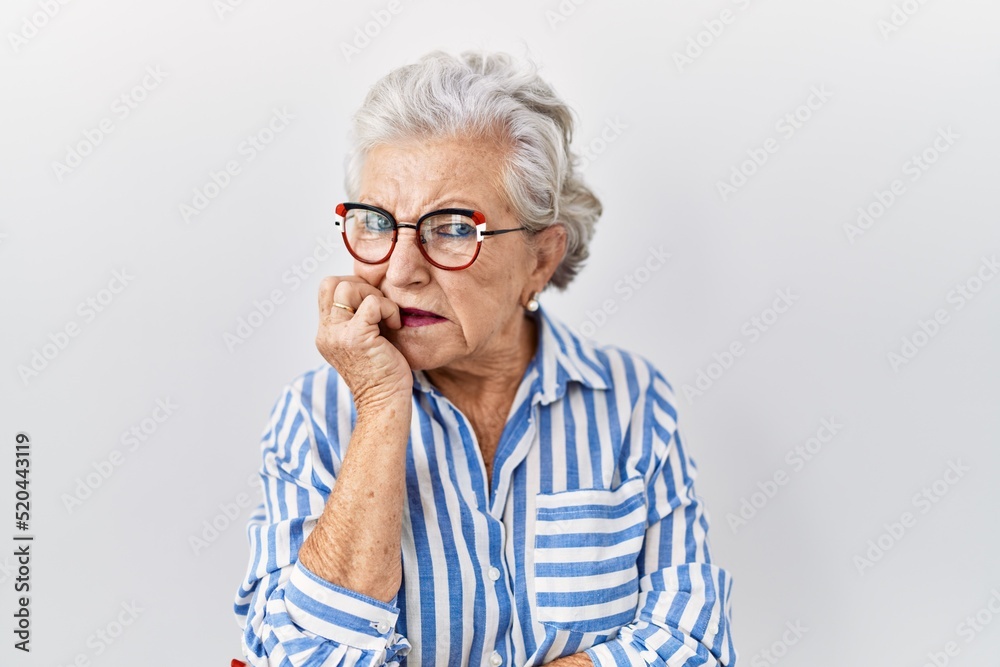 Senior woman with grey hair standing over white background looking stressed and nervous with hands on mouth biting nails. anxiety problem.
