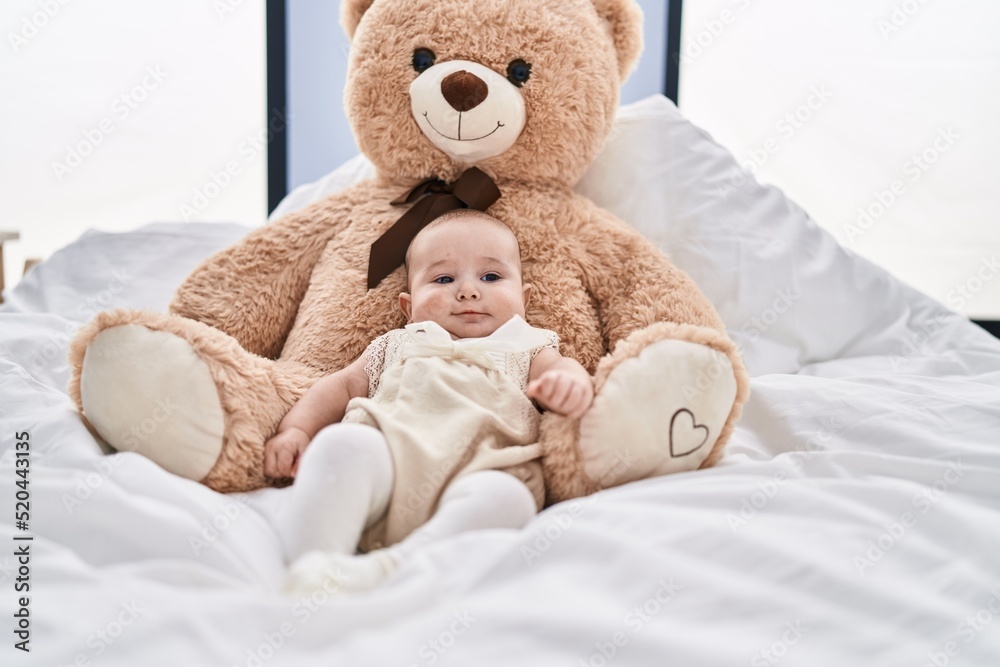 Adorable baby relaxed lying on bed with teddy bear at bedroom