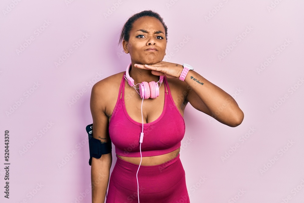 Young african american girl wearing gym clothes and using headphones cutting throat with hand as knife, threaten aggression with furious violence