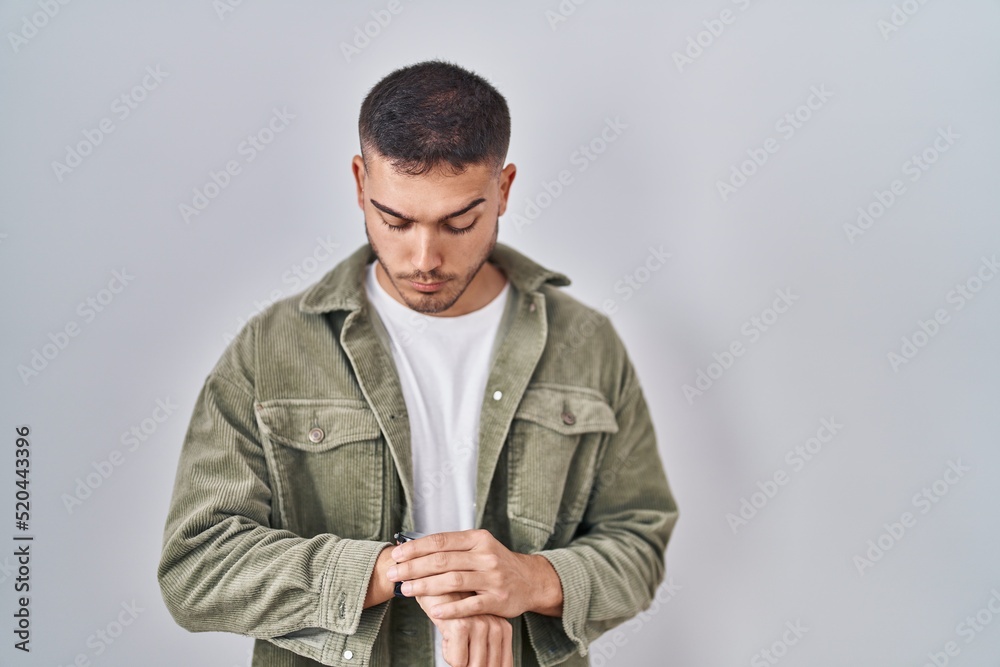 Young hispanic man standing over isolated background checking the time on wrist watch, relaxed and confident Young hispanic man standing over isolated background checking the time on wrist watch, relaxed and confident