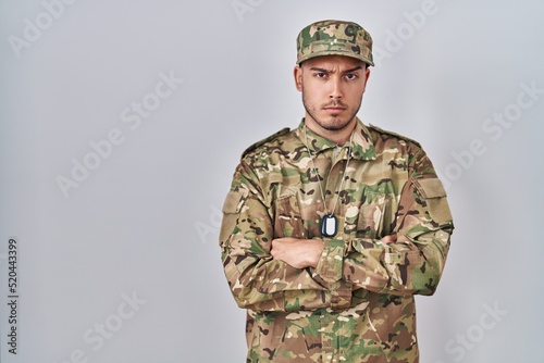 Young hispanic man wearing camouflage army uniform skeptic and nervous, disapproving expression on face with crossed arms. negative person.