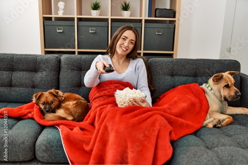 Photography Young hispanic woman watching movie sitting on sofa with dogs at home