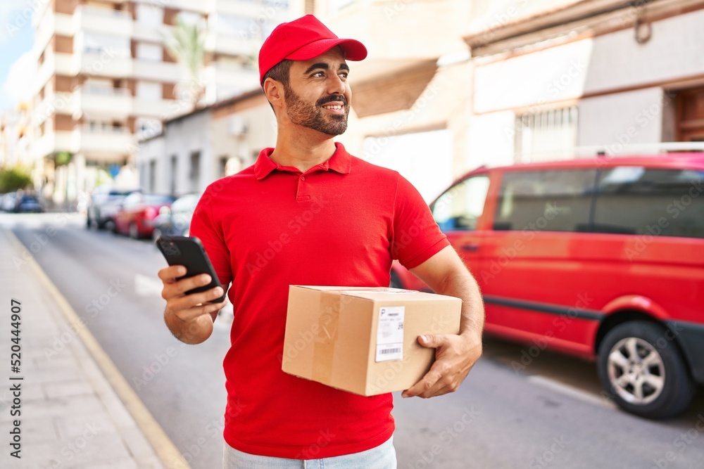 Young hispanic man courier using smartphone holding package at street Young hispanic man courier using smartphone holding package at street