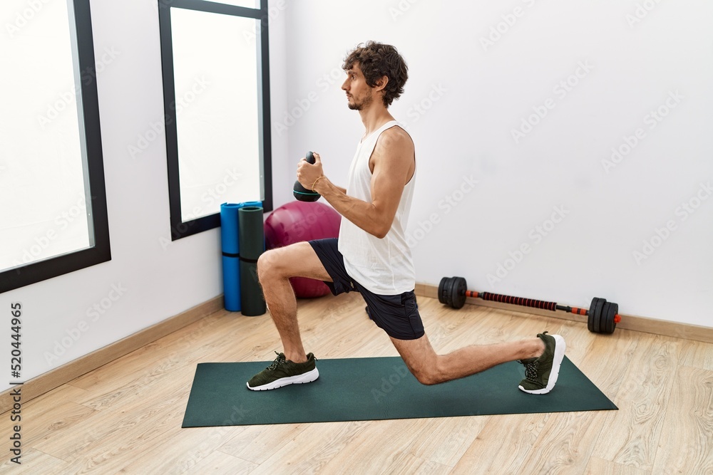 Young hispanic man training using kettlebell at sport center