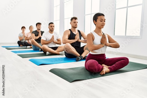 Group of young hispanic people concentrated training yoga at sport center.