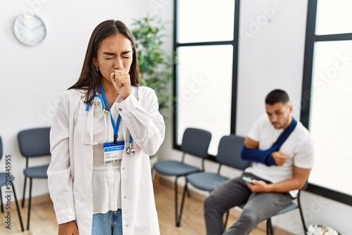 Young asian doctor woman at waiting room with a man with a broken arm feeling unwell and coughing as symptom for cold or bronchitis. health care concept.