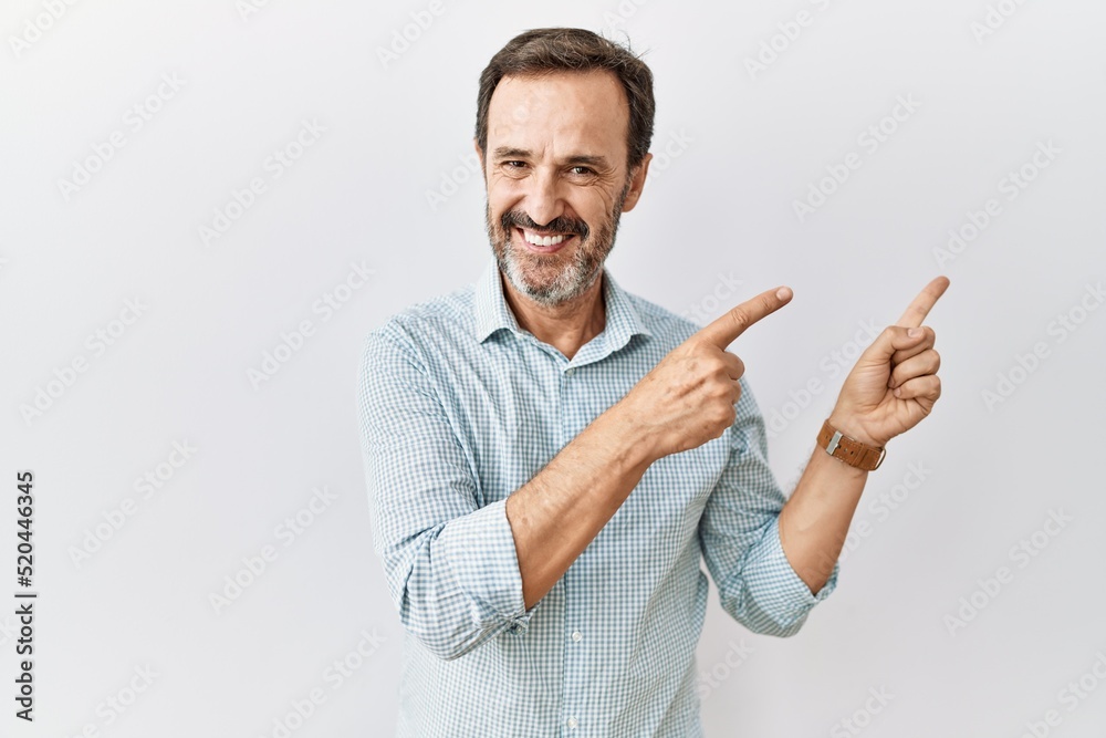 Middle age hispanic man with beard standing over isolated background smiling and looking at the camera pointing with two hands and fingers to the side. Middle age hispanic man with beard standing over isolated background smiling and looking at the camera pointing with two hands and fingers to the side.