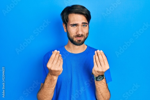 Young hispanic man wearing casual clothes doing money gesture with hands, asking for salary payment, millionaire business