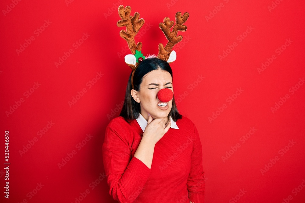 Young hispanic woman wearing deer christmas hat and red nose touching painful neck, sore throat for flu, clod and infection Young hispanic woman wearing deer christmas hat and red nose touching painful neck, sore throat for flu, clod and infection