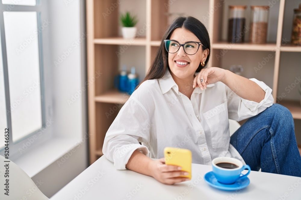 Young hispanic woman using smartphone drinking coffee at home Young hispanic woman using smartphone drinking coffee at home