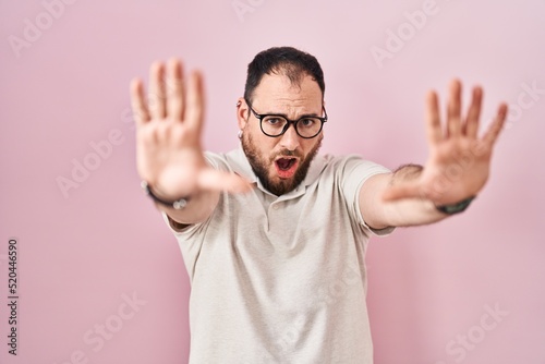 Plus size hispanic man with beard standing over pink background doing stop gesture with hands palms, angry and frustration expression