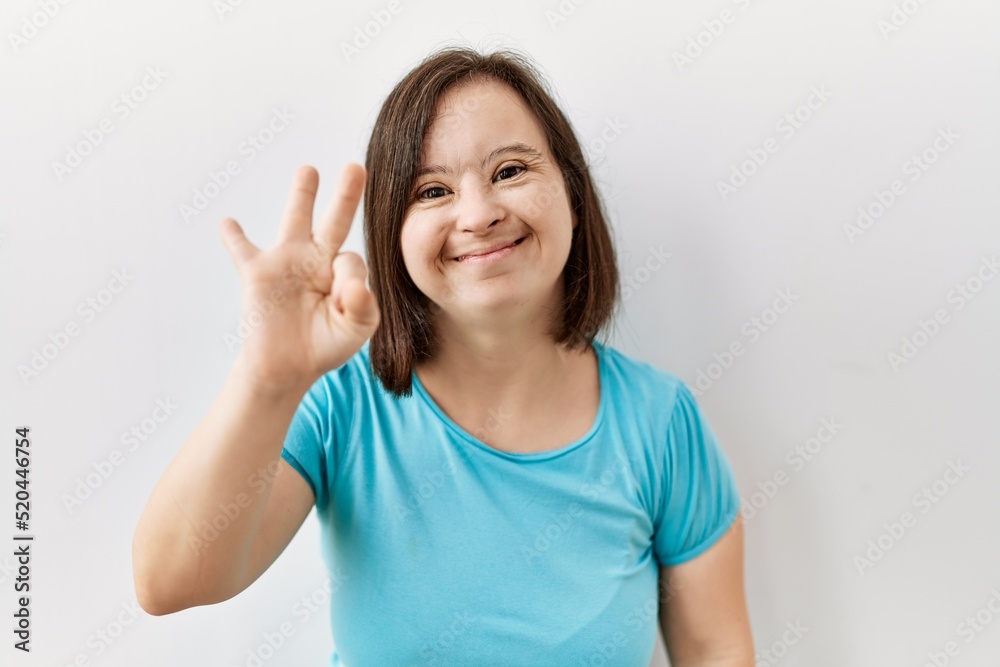 Young down syndrome woman standing over isolated background showing and pointing up with fingers number three while smiling confident and happy. Young down syndrome woman standing over isolated background showing and pointing up with fingers number three while smiling confident and happy.