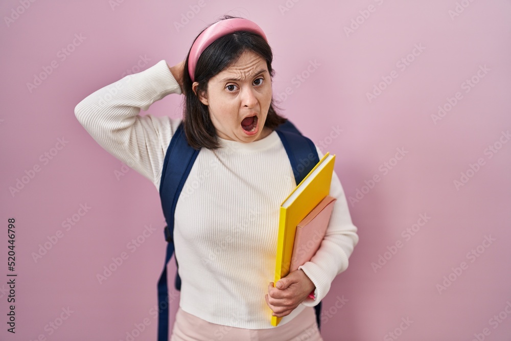 Woman with down syndrome wearing student backpack and holding books crazy and scared with hands on head, afraid and surprised of shock with open mouth Woman with down syndrome wearing student backpack and holding books crazy and scared with hands on head, afraid and surprised of shock with open mouth