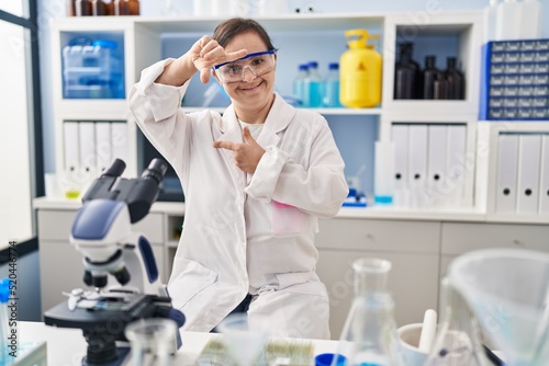 Hispanic girl with down syndrome working at scientist laboratory smiling making frame with hands and fingers with happy face. creativity and photography concept.