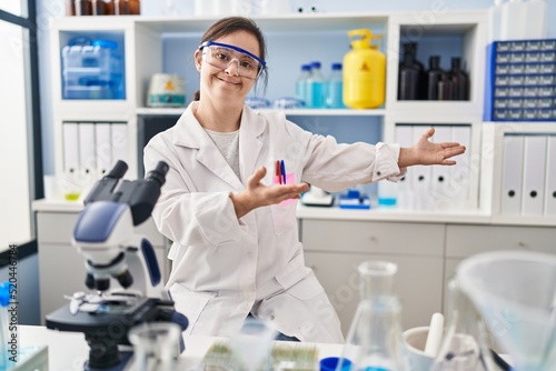 Hispanic girl with down syndrome working at scientist laboratory inviting to enter smiling natural with open hand