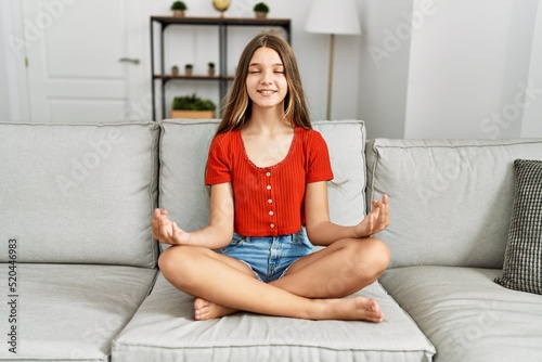 Adorable girl doing yoga exercise sitting on sofa at home
