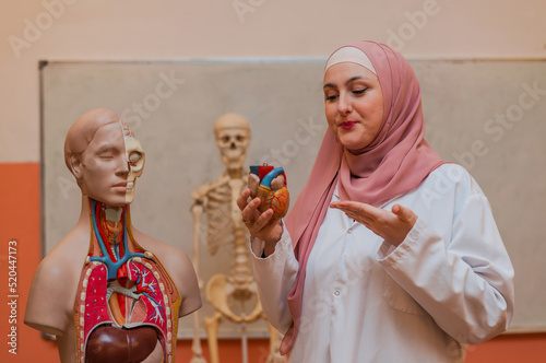 A Muslim female teacher uses the human body model to explain anatomy in biology class in the classroom lab. photo
