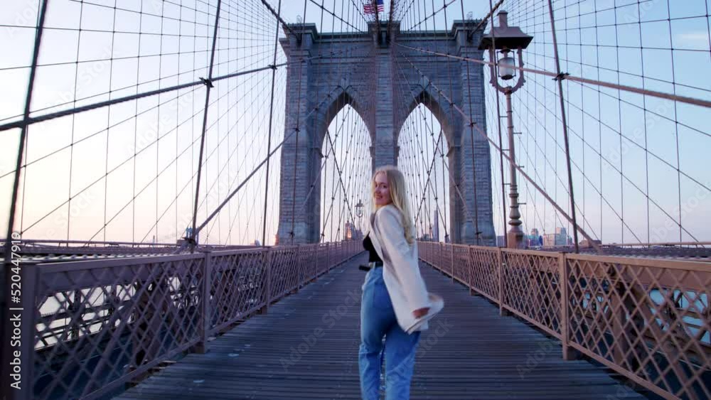 Astonishing cityscape with tall skyscrapers beyond bluish skyline. Back view of a blonde-haired female tourist running along iconic landmark of New York City, USA. High quality 4k footage