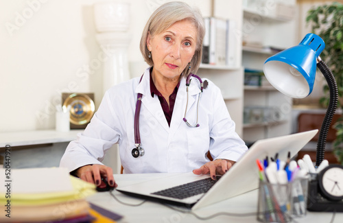 Portrait of confident mature female doctor working with papers and laptop at medical office