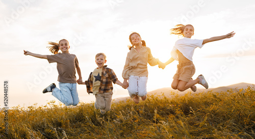 Group of happy joyful school kids boys and girls jumping with holding hands in field on sunny day