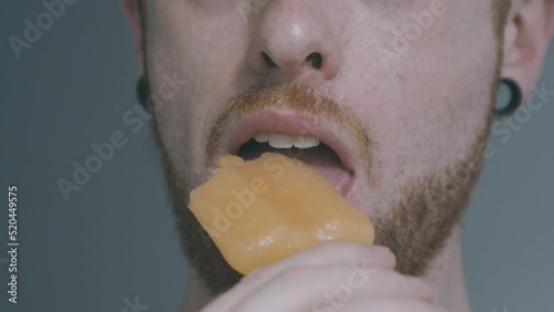 A boy with ear dilators stacks the camera with a peach popsicle, and then approaches the popsicle and eats it photo