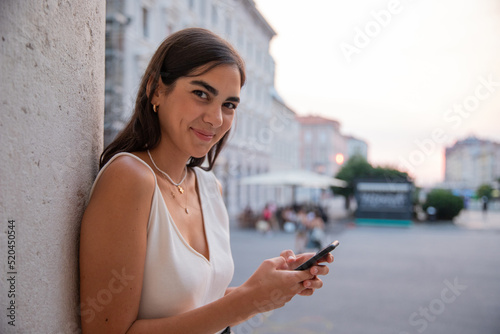 Young girl in town leaning against a message pole with her cell phone