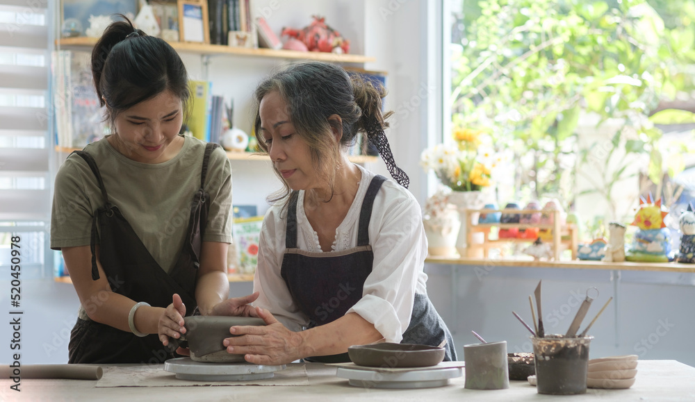 Middle age woman with her .daughter standing in pottery workshop. Creative activities, pottery, workshop, ceramics art concept. Middle age woman with her .daughter standing in pottery workshop. Creative activities, pottery, workshop, ceramics art concept.