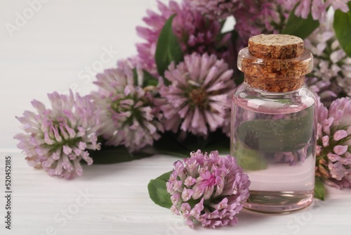 Beautiful clover flowers and essential oil on white wooden table, closeup. Space for text