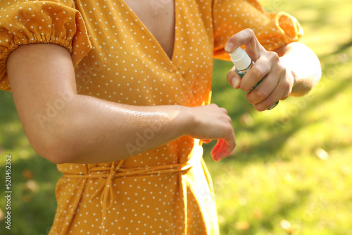 Woman applying insect repellent onto hand in park, closeup photo