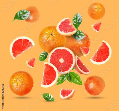 Tasty ripe grapefruits and green leaves falling on orange background