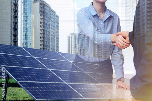 Double exposure of businesspeople shaking hands and solar panels installed outdoors. Alternative energy source photo