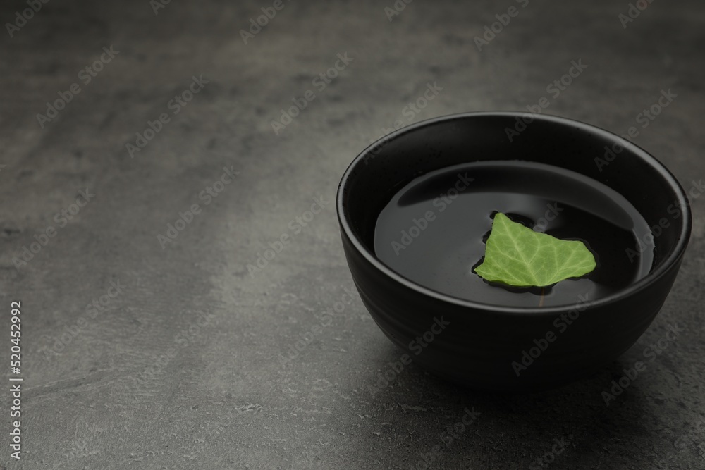 Black bowl with water and green leaf on grey table. Space for text Black bowl with water and green leaf on grey table. Space for text