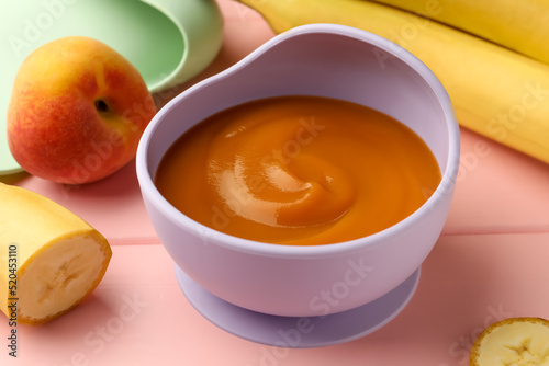 Healthy baby food in bowl and fresh fruits on pink wooden table, closeup