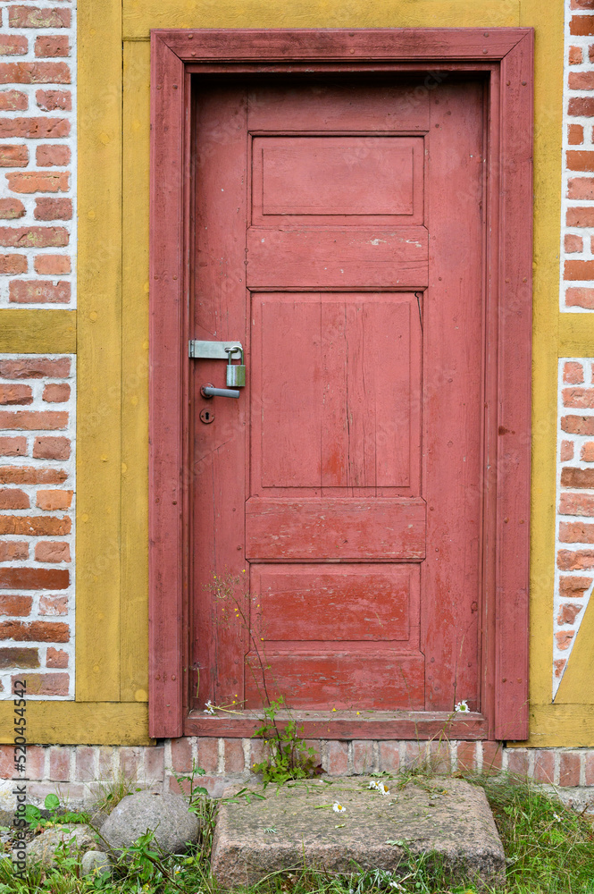 Red wood door, locked with a padlock, of a red brick and wood building
Red wood door, locked with a padlock, of a red brick and wood building
