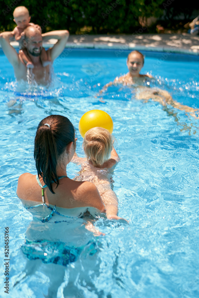Parents with small kids playing with a ball in the pool